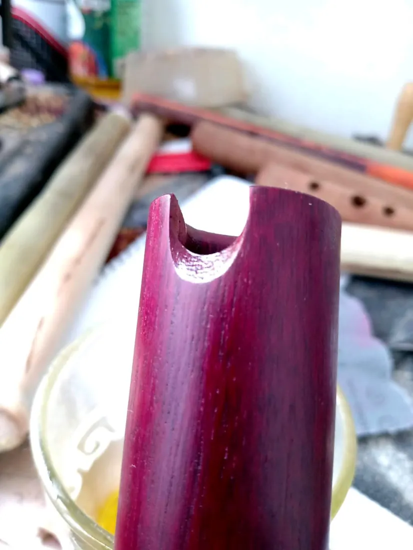 Quena en madera de nazareno. Luce su color rojizo. Es sostenida por la mano del luthier.